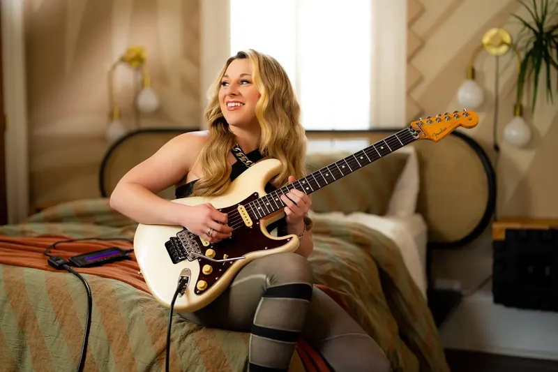 Alyssa Day playing electric guitar on a sofa while recording with the Fender Studio app