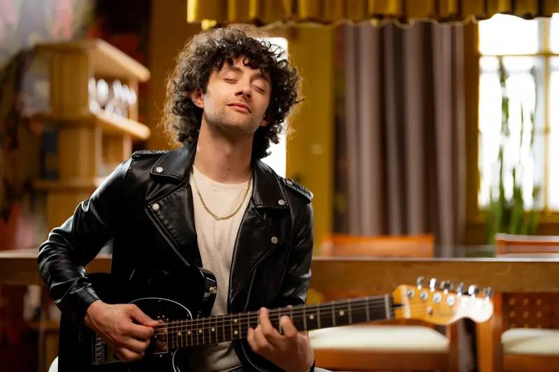 Dre Dimura seated with an electric guitar in a warm interior for the Fender Studio app campaign